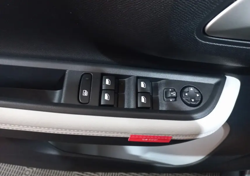 Gros plan sur la commande des vitres et rétroviseurs côté conducteur de la Citroën C3 hybride gris foncé avec surpiqûres blanches et étiquette rouge "be cool".