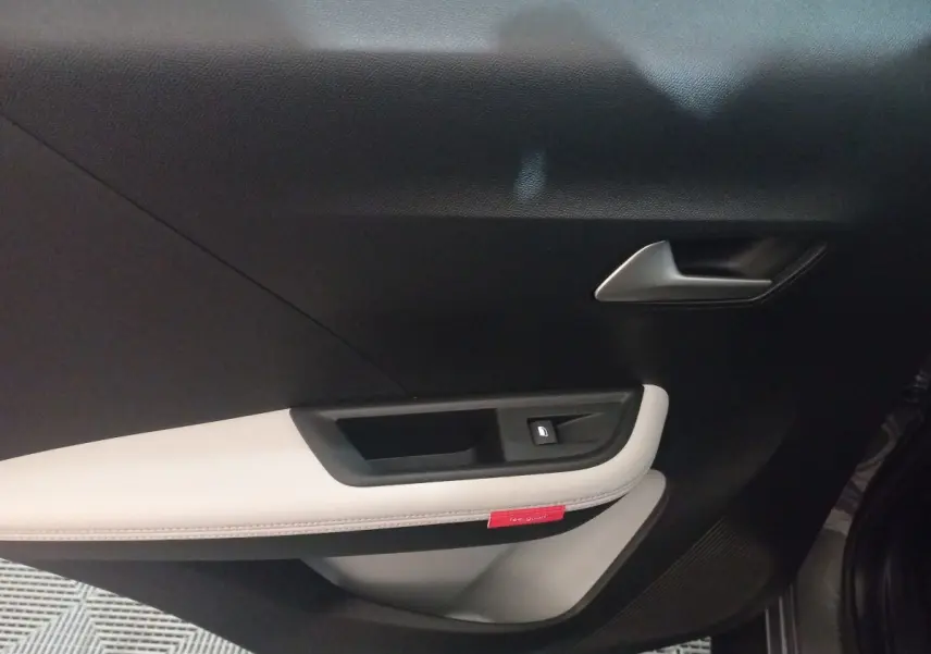 Gros plan sur la porte intérieure côté droit de la Citroën C3 hybride 2025, avec garniture noire et beige et bouton de fenêtre.