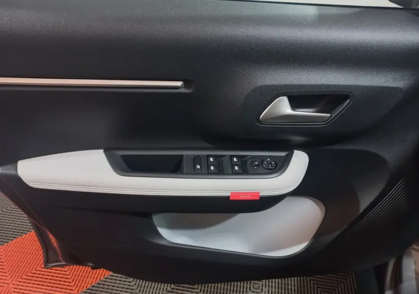 Vue rapprochée de la porte côté conducteur de la Citroën C3 hybride 2025, avec garniture noire et blanche et commandes électriques.
