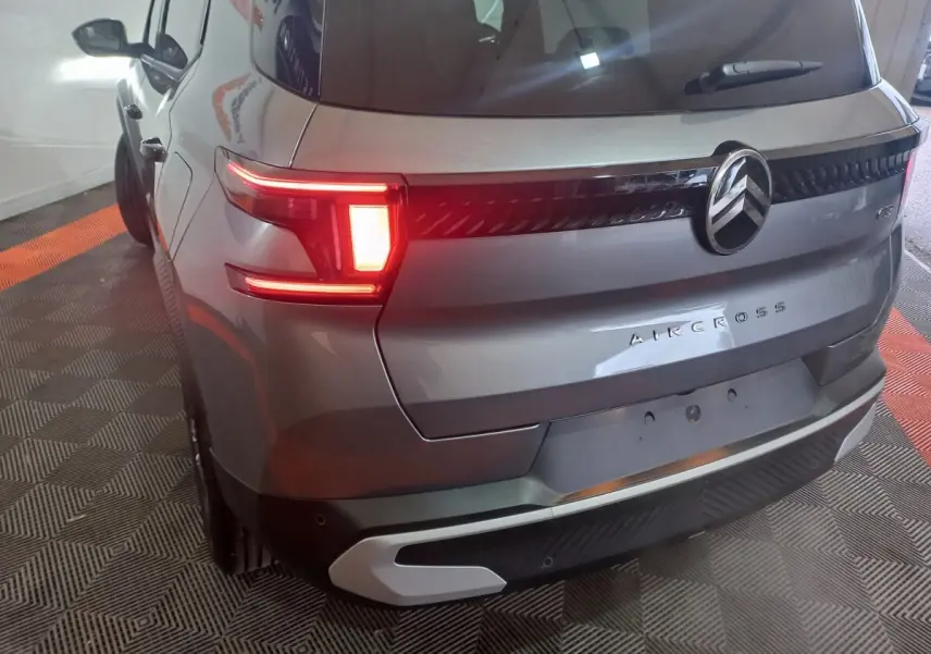 Vue 3/4 arrière droite d'un Citroën Aircross gris foncé avec feux arrière allumés et logo central visible.