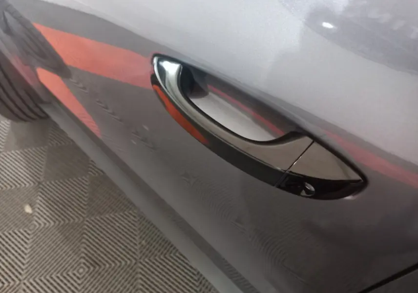 Poignée de porte côté gauche sur Citroën C3 hybride gris foncé, vue rapprochée mettant en valeur la finition brillante.