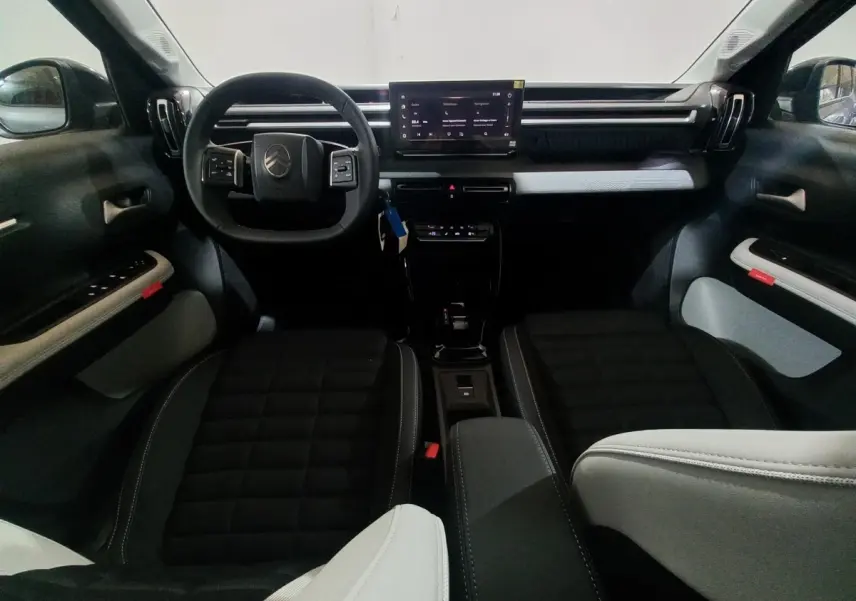 Vue intérieure avant du Citroën C3 hybride 2025, tableau de bord noir avec écran tactile central et sièges bi-ton noirs et gris.