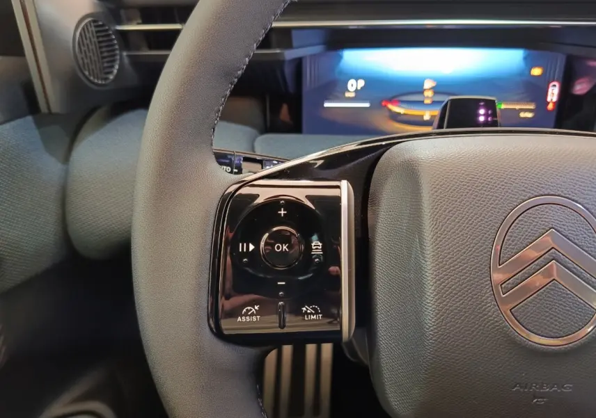 Vue rapprochée du volant cuir gris de la Citroën C5 Hybride avec commandes multifonctions et tableau de bord numérique éclairé.
