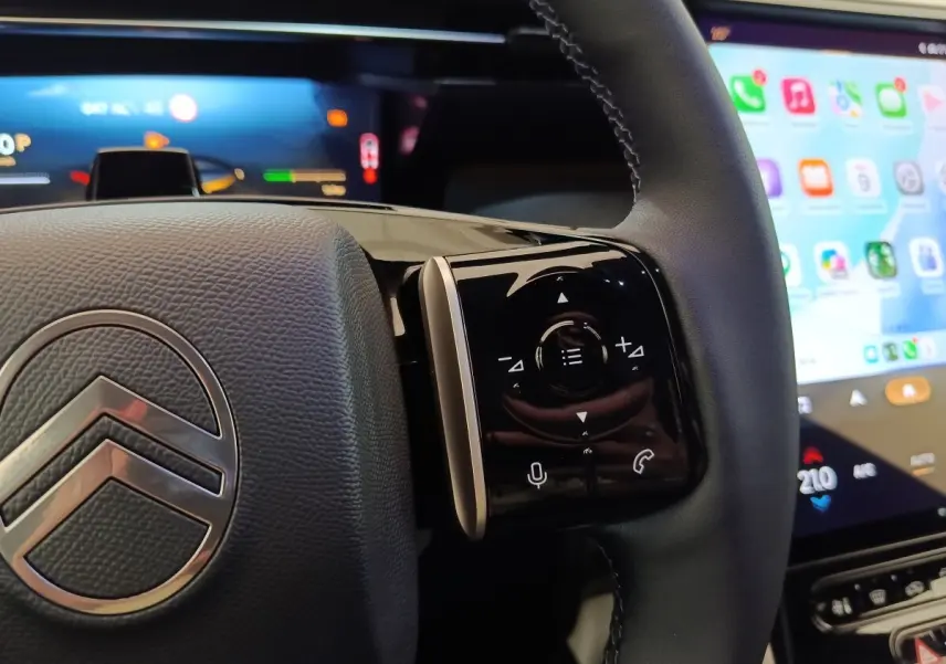 Gros plan sur le volant cuir noir de la Citroën C5 hybride 2026 avec commandes multifonctions et écran tactile en arrière-plan.