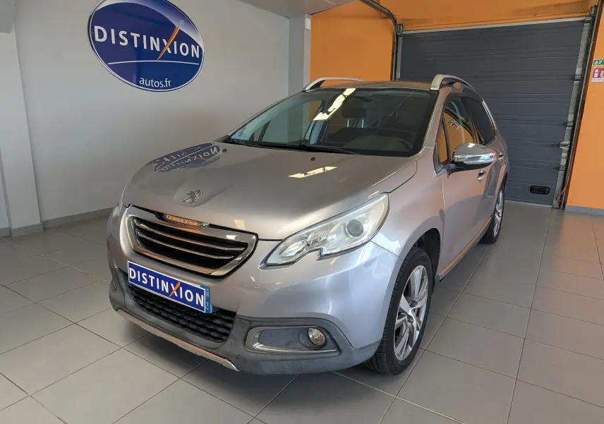 Peugeot 2008 gris artense en 3/4 avant droit dans un showroom avec logo Distinxion en arrière-plan.