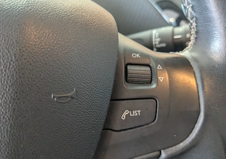 Gros plan sur les commandes noires du volant de la Peugeot 2008 gris artense, avec boutons OK et LIST visibles.