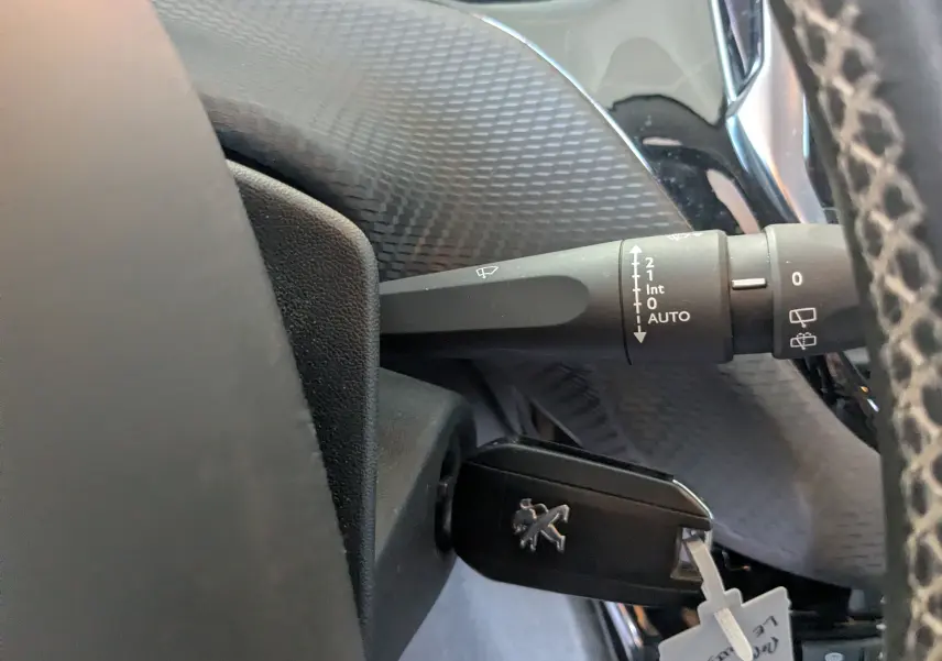 Gros plan sur la commande d'essuie-glace et la clé insérée dans le contacteur d'un Peugeot 2008 gris Artense, intérieur noir.