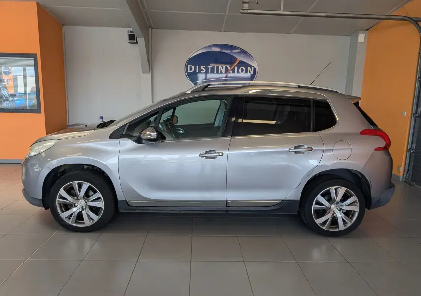 Vue de profil côté gauche d’un Peugeot 2008 gris Artense, SUV compact avec jantes alliage et barres de toit visibles.