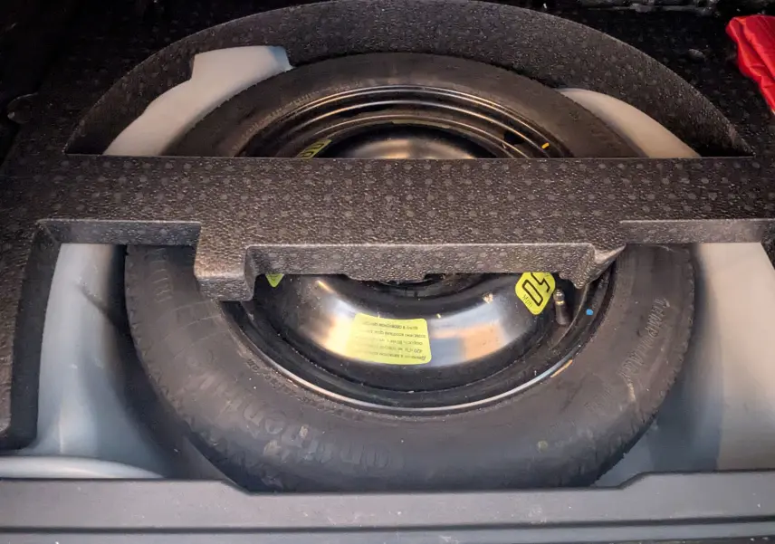 Vue rapprochée de la roue de secours noire logée dans le coffre d'une Peugeot 2008 gris Artense de 2015.