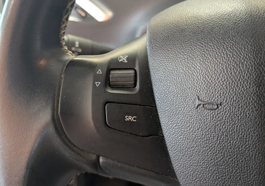 Gros plan sur les commandes audio au volant noir du Peugeot 2008 gris Artense, version 2015 diesel.