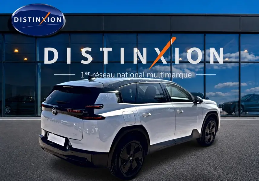 Vue 3/4 arrière droite du Citroën C5 Aircross blanc à toit noir avec jantes alliage noires devant une vitrine Distinxion.