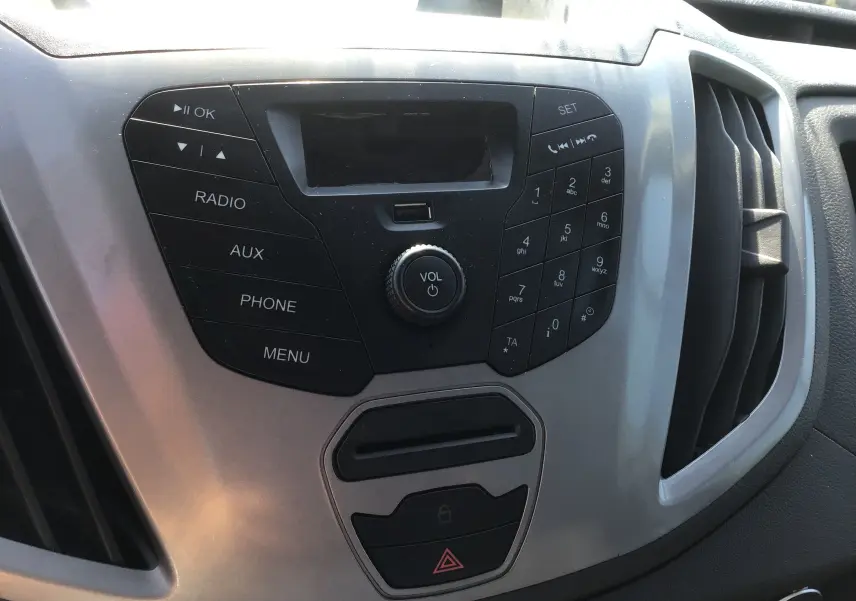 Vue rapprochée du tableau de bord central du Ford Transit Chassis Cabine blanc, avec commandes radio et ventilation.