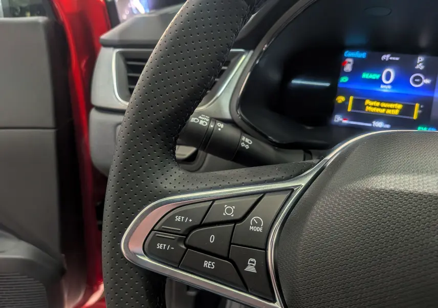 Gros plan sur le volant perforé et les commandes multifonctions du Renault Captur E-TECH rouge Flamme, tableau de bord numérique visible.