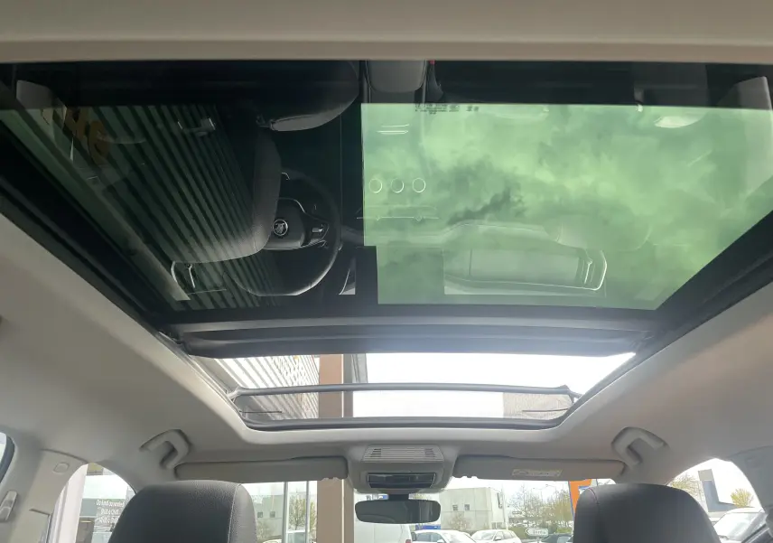 Vue intérieure du toit ouvrant panoramique du Skoda Kodiaq noir métal 2024, avec reflet du ciel et volant visible.