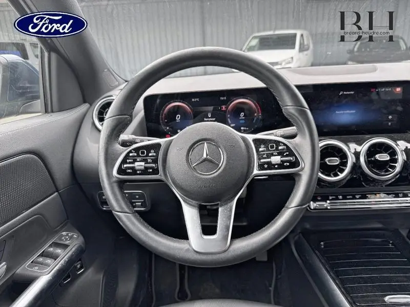 Vue intérieure centrée sur le volant cuir multifonction d'une Mercedes GLA 250 e bleu denim avec tableau de bord numérique.