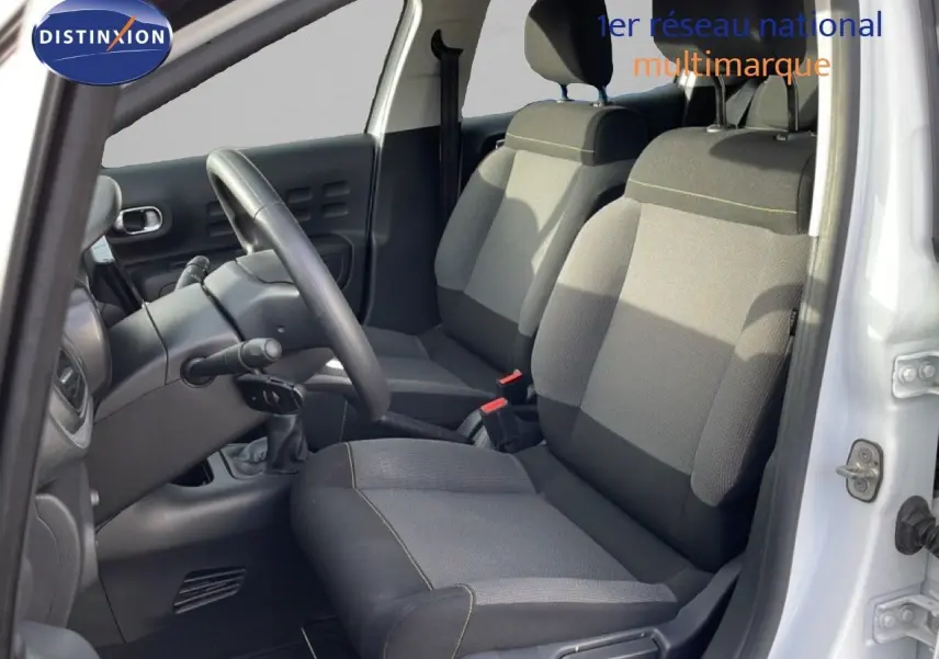 Vue intérieure côté conducteur de la Citroën C3 blanche avec toit rouge, montrant les sièges avant en tissu gris et volant noir.