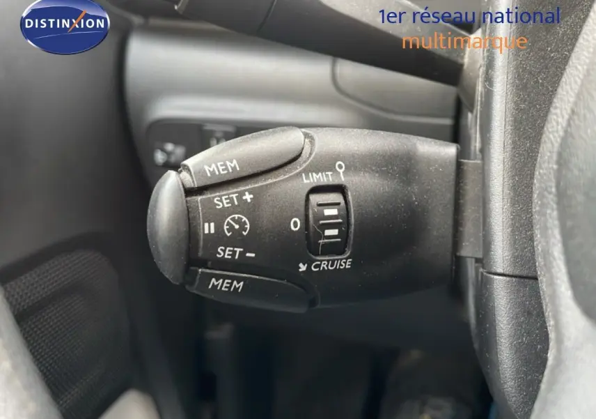 Gros plan sur la commande de régulateur de vitesse à gauche du volant d'une Citroën C3 blanc toit rouge, intérieur noir.