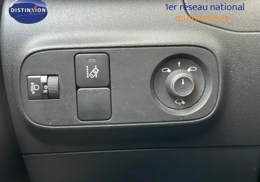 Gros plan sur les commandes de réglage des rétroviseurs et des phares d’une Citroën C3 blanche toit rouge, intérieur noir.