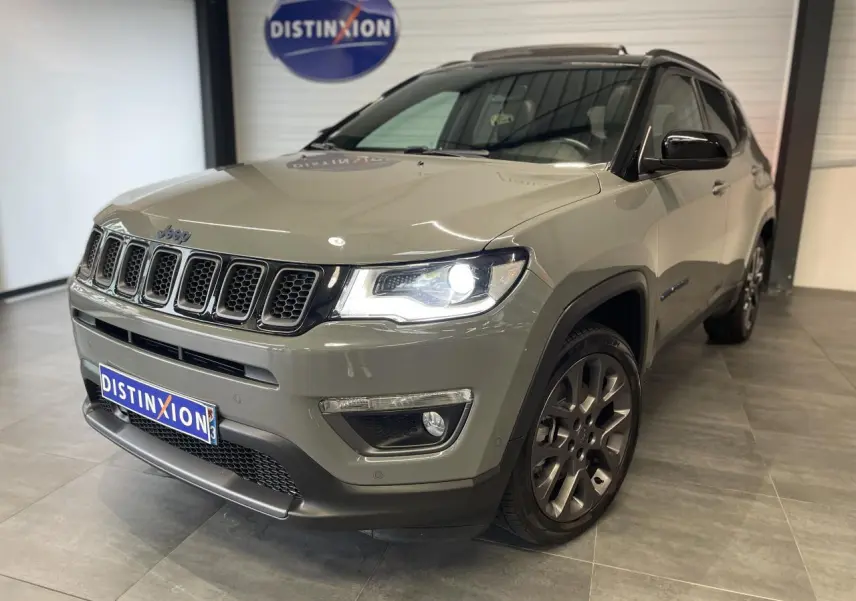 Jeep Compass gris foncé en 3/4 avant droit avec phares allumés et jantes alliage 17 pouces en showroom.