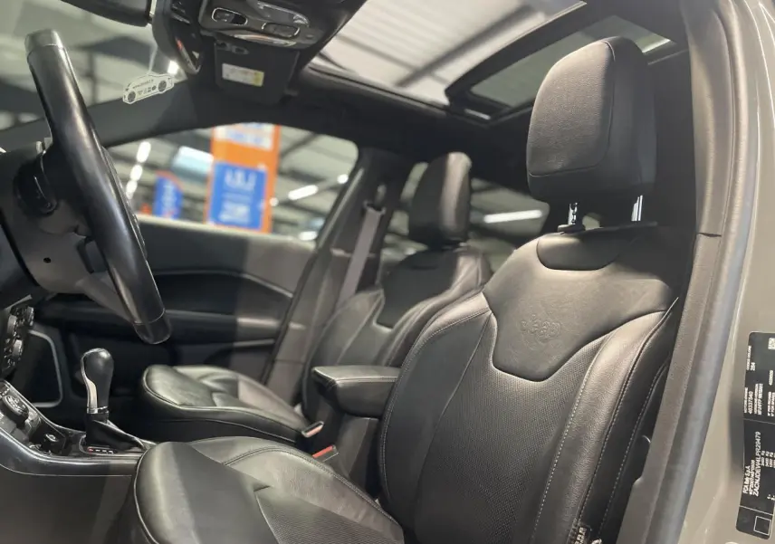 Vue intérieure côté conducteur du Jeep Compass gris foncé, mettant en valeur les sièges cuir noirs et le toit ouvrant panoramique.