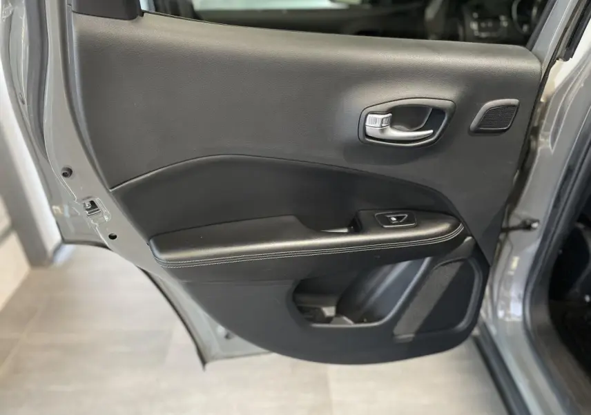 Vue rapprochée de la porte arrière droite ouverte d’un Jeep Compass gris foncé, avec garniture intérieure noire.
