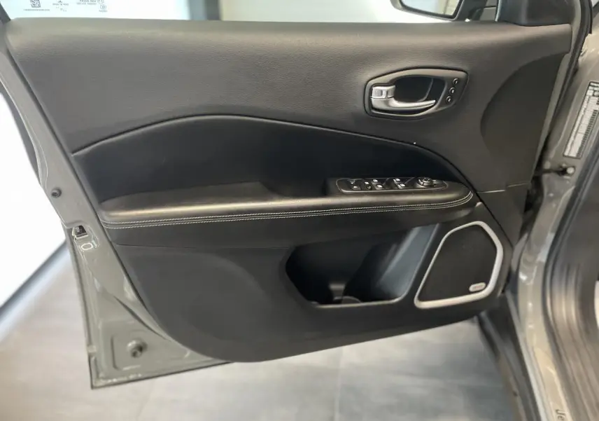 Vue rapprochée de la porte avant gauche gris foncé du Jeep Compass avec commandes électriques et haut-parleur intégré.