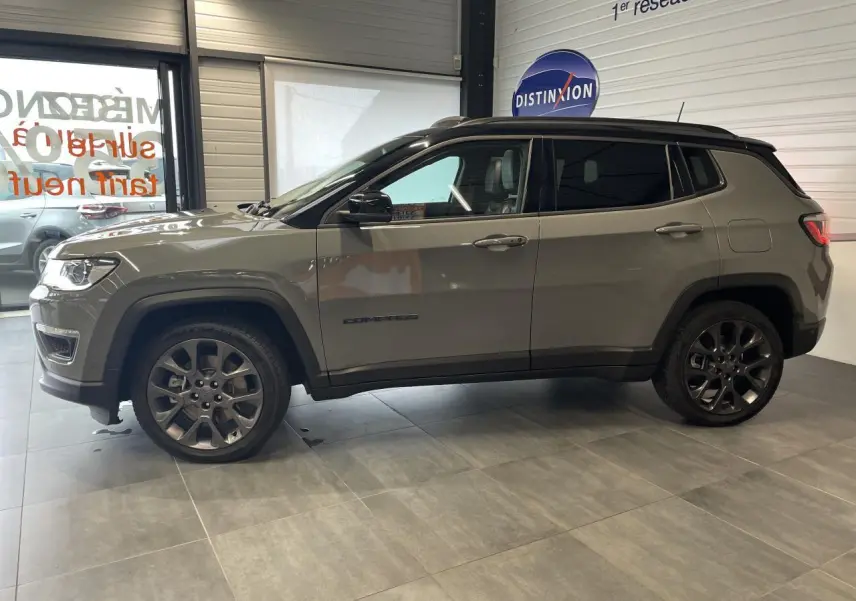 Vue de profil côté gauche d'un Jeep Compass gris foncé avec jantes alliage et vitres arrière surteintées en intérieur showroom.