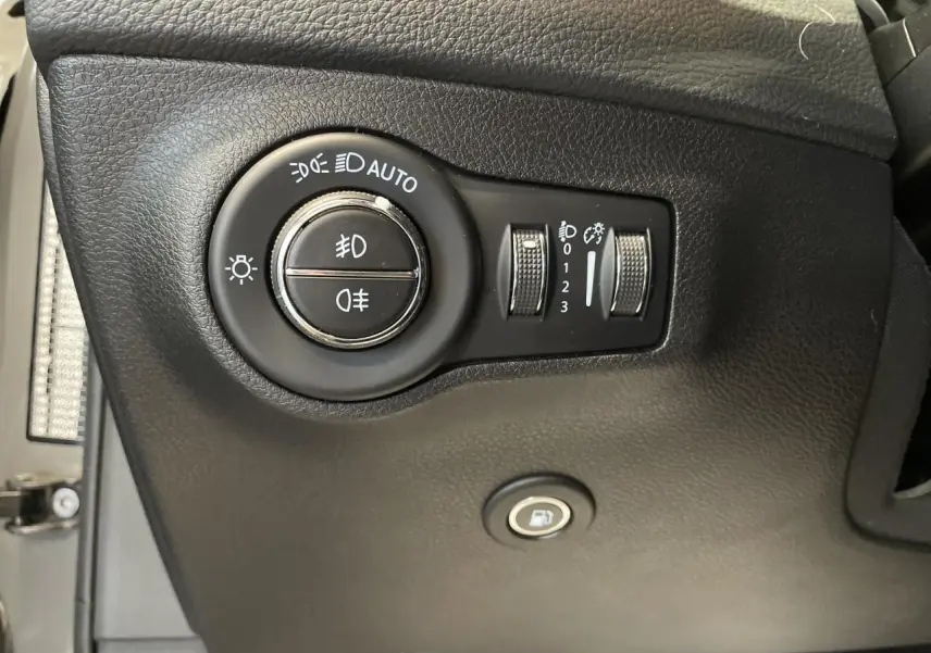Gros plan sur les commandes d'éclairage et ouverture de trappe à carburant du Jeep Compass gris foncé, intérieur noir.