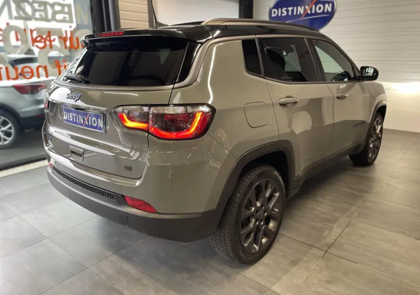 Vue 3/4 arrière droit d'un Jeep Compass gris foncé avec feux arrière allumés et toit noir en intérieur showroom.