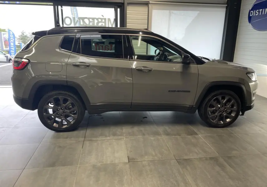 Vue de profil côté gauche d’un Jeep Compass gris foncé avec jantes alliage et vitres surteintées en intérieur showroom.