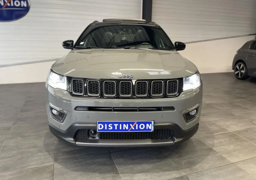 Vue avant d'un Jeep Compass gris foncé avec calandre à sept fentes et phares LED allumés en intérieur showroom.