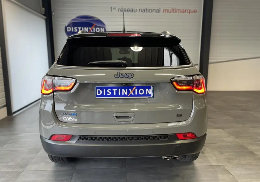 Vue arrière d'un Jeep Compass gris foncé avec feux allumés et double sortie d'échappement visible en intérieur showroom.