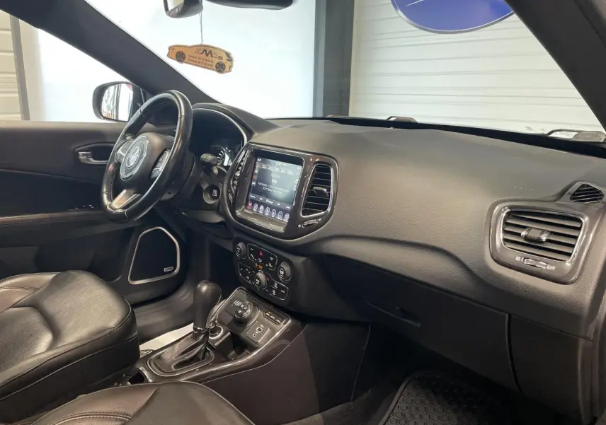 Intérieur avant droit du Jeep Compass gris foncé, avec tableau de bord tactile et sellerie cuir noire.
