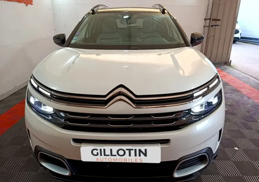 Vue avant d'un Citroën C5 Aircross Hybrid blanc avec phares LED allumés dans un showroom.