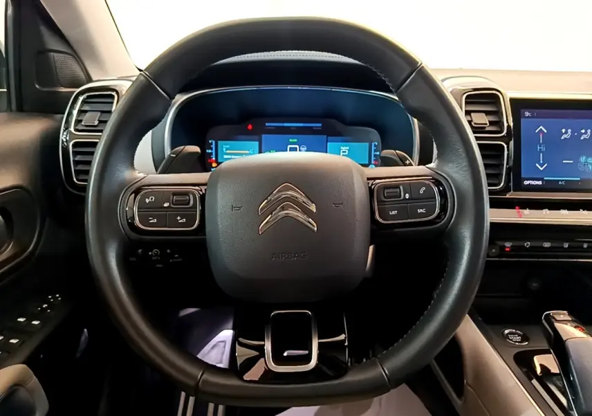 Vue intérieure centrée sur le volant cuir noir du Citroën C5 Aircross Hybrid 225 ë-EAT8 avec tableau de bord digital.