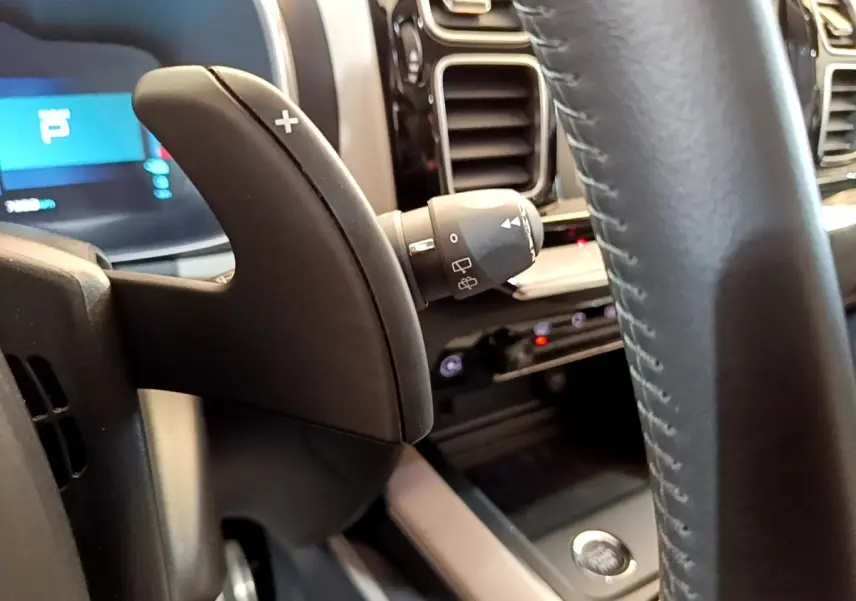 Gros plan sur la palette de changement de vitesse droite et le volant cuir du tableau de bord du Citroën C5 Aircross Hybrid blanc.