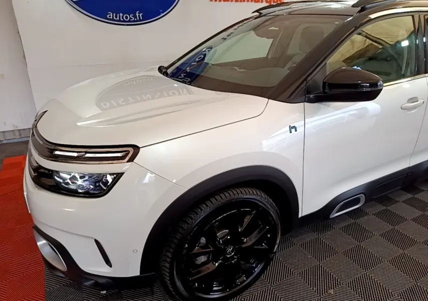 Vue 3/4 avant droit d'un Citroën C5 Aircross Hybrid blanc avec jantes noires et toit noir brillant.