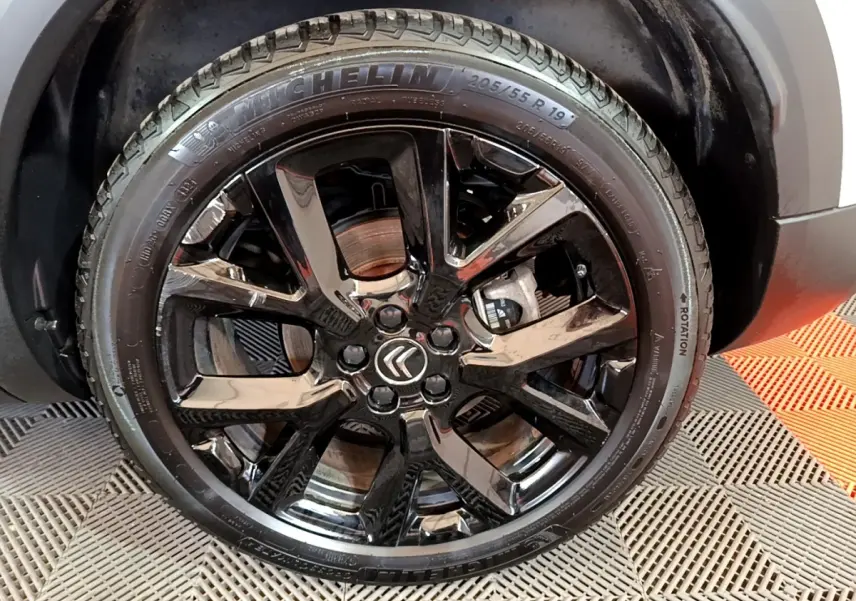 Gros plan sur la roue avant droite noire brillante du Citroën C5 Aircross Hybrid 225 ë-EAT8 Shine Pack blanc.