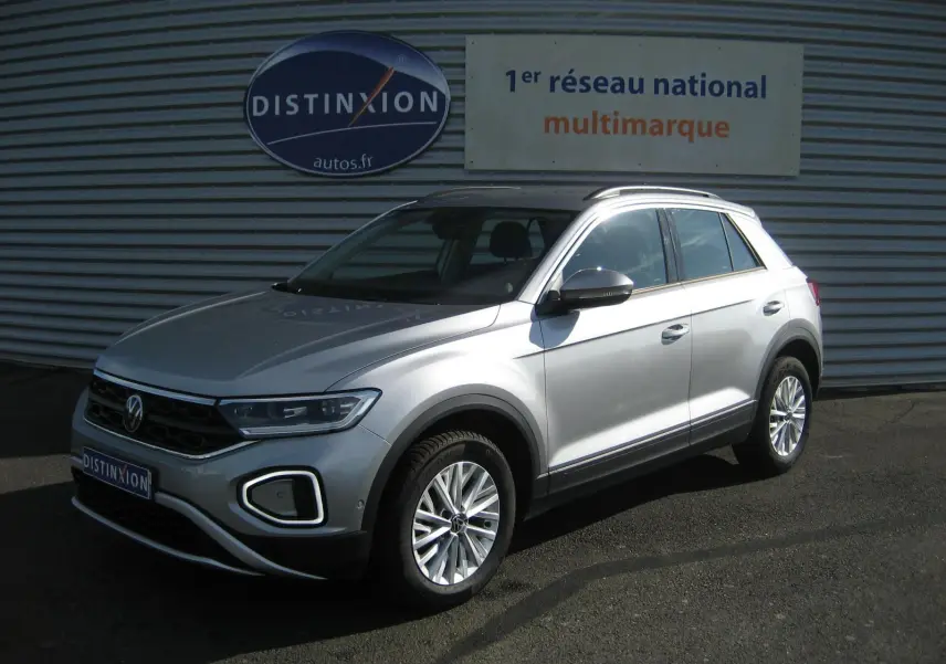 Volkswagen T-Roc gris clair vu en 3/4 avant droit, avec jantes alliage et calandre noire distinctive.