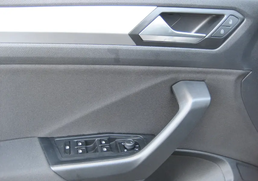 Vue rapprochée de la porte côté gauche du Volkswagen T-Roc gris clair, montrant les commandes des vitres et des rétroviseurs.