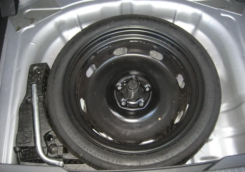 Vue en plongée sur la roue de secours noire et les outils dans le coffre d’un Volkswagen T-Roc gris clair 2023.