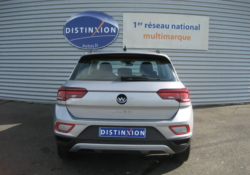 Vue arrière d’un Volkswagen T-Roc gris clair 2023 avec feux LED et logo distinctif sur fond de façade métallique.