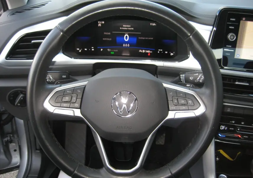 Vue rapprochée du volant noir du Volkswagen T-Roc 2023 avec tableau de bord numérique et écran tactile visible.