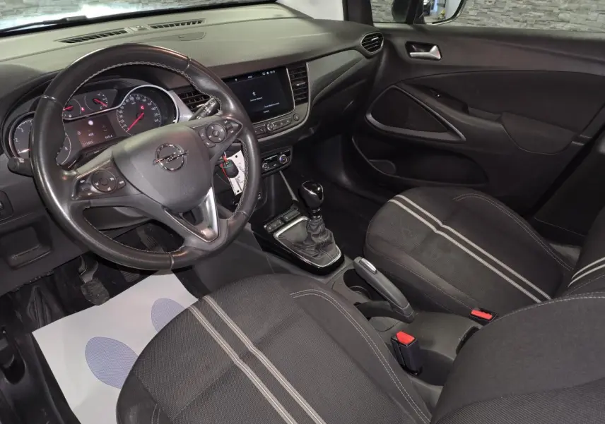 Vue intérieure côté conducteur de l'Opel Crossland 2023 avec sellerie tissu noire à bandes grises et tableau de bord noir.