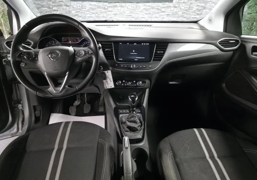 Intérieur avant de l'Opel Crossland gris 2023, vue centrée sur le tableau de bord et la boîte manuelle noire.