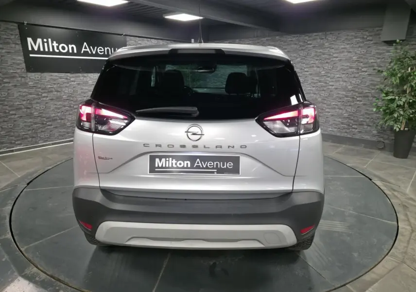 Vue arrière d'un Opel Crossland gris métallisé 2023 avec feux arrière allumés et logo central sur fond intérieur showroom.