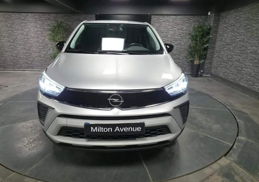 Vue avant d'un Opel Crossland gris métallisé 2023 avec calandre noire et phares LED allumés dans un showroom.