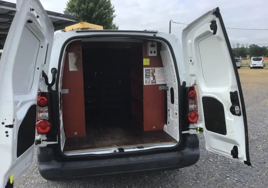 Vue arrière d’un Citroën Berlingo XL blanc 2018 avec portes ouvertes montrant l’intérieur aménagé de rangements en bois.