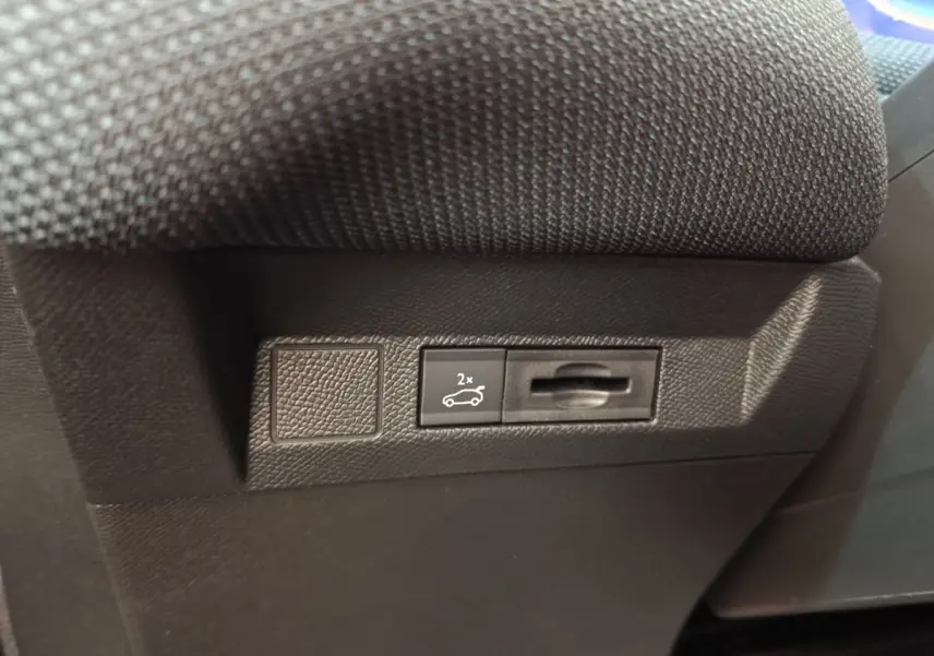 Gros plan sur le bouton d'ouverture du coffre noir, situé sous le siège d'une Citroën C5 hybride verte.
