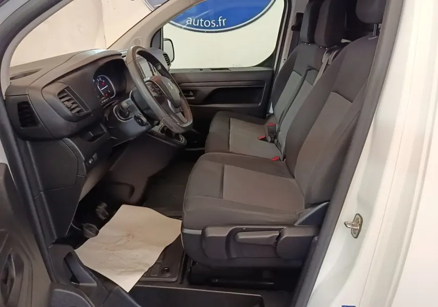Vue intérieure côté conducteur du Peugeot Expert Fourgon blanc, montrant les sièges avant et le tableau de bord noir.